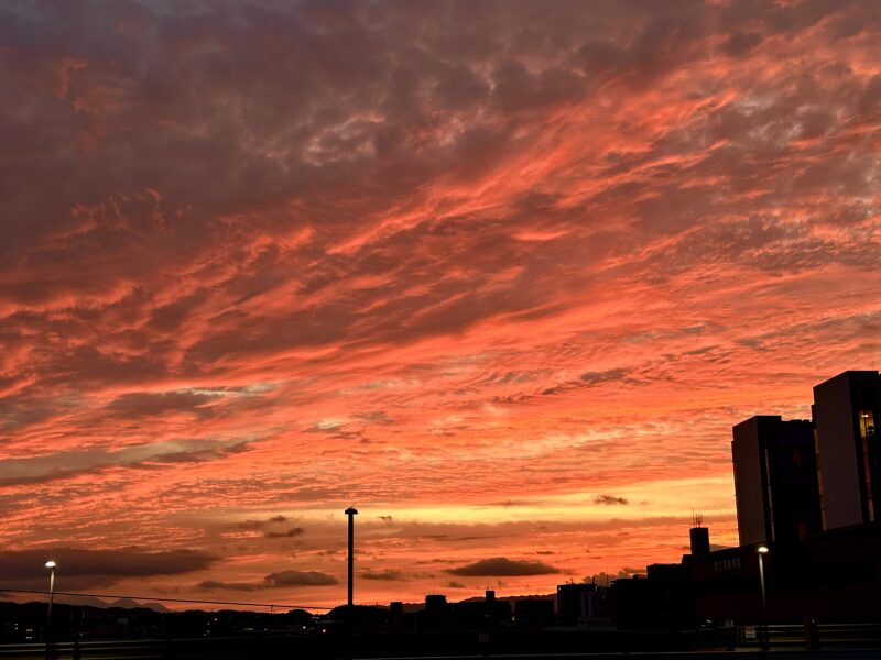 陸橋から見下ろす都市の向こうに、茜色と黒い山脈がコントラストを描く夕焼け空